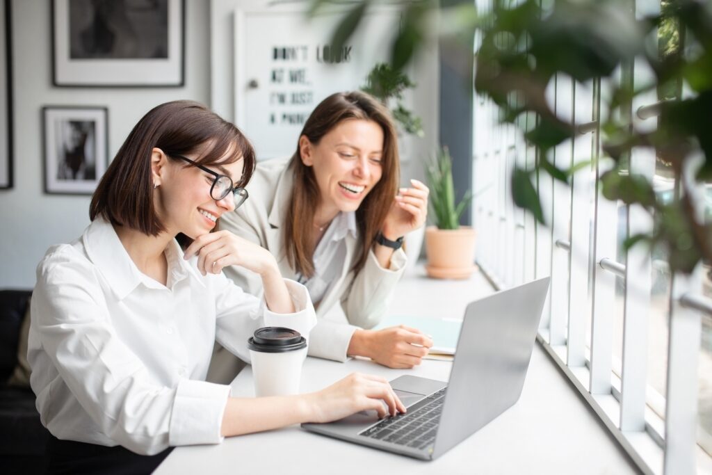 Two women collaborating at a laptop during a productivity coaching session, illustrating how to optimize time for increased productivity and freedom.