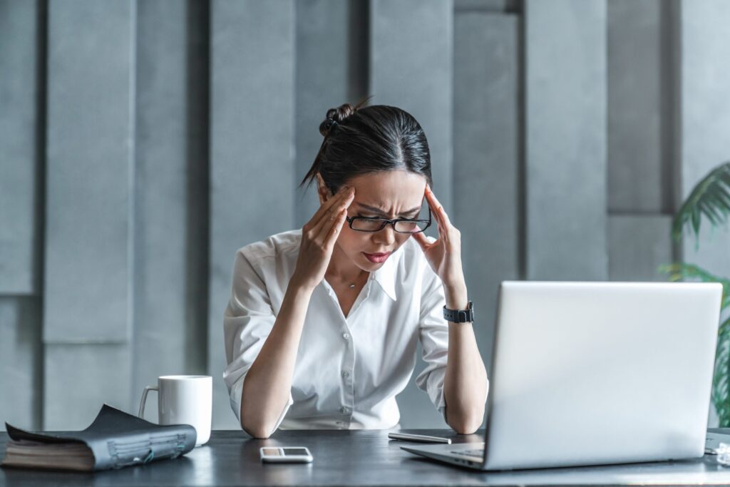 Stressed woman holding her head in frustration while working on her laptop, representing the struggle of learning how to believe in yourself during difficult times.
