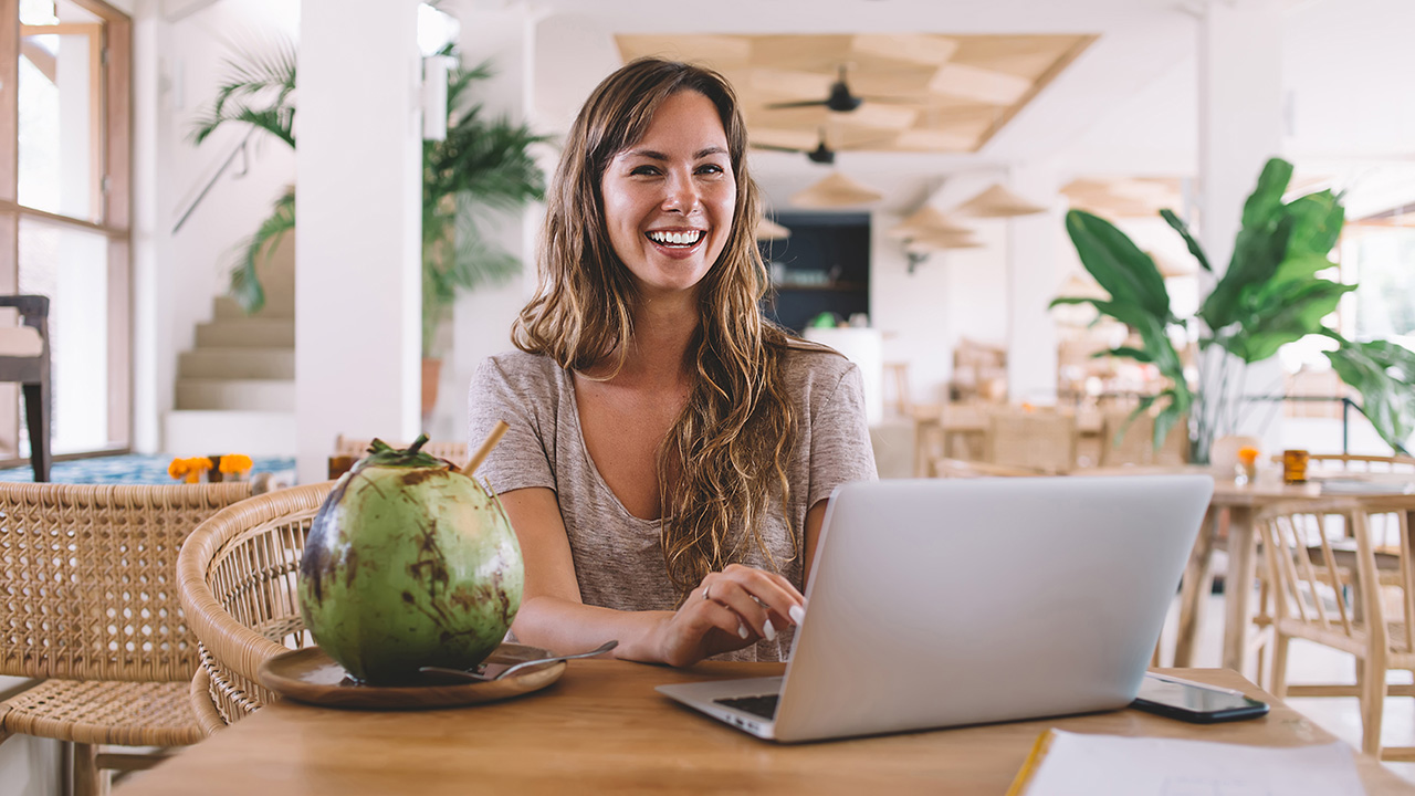 Smiling woman working on a laptop with a coconut drink, representing productivity, balance, and the use of high performance habits tools for success.