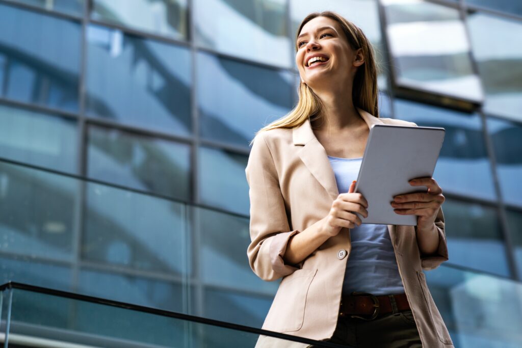 Smiling Professional Woman Holding a Tablet Outdoors Representing Confidence Optimism and the Growth focused Attitude of a High Performance Mindset