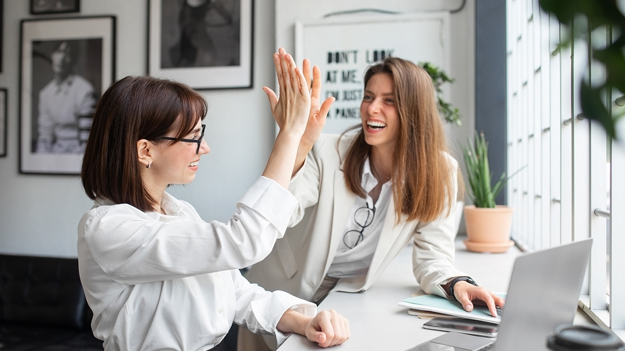 Two professional women celebrating success with a high-five, representing teamwork, positivity, and strategies for how to stay motivated in business and life.