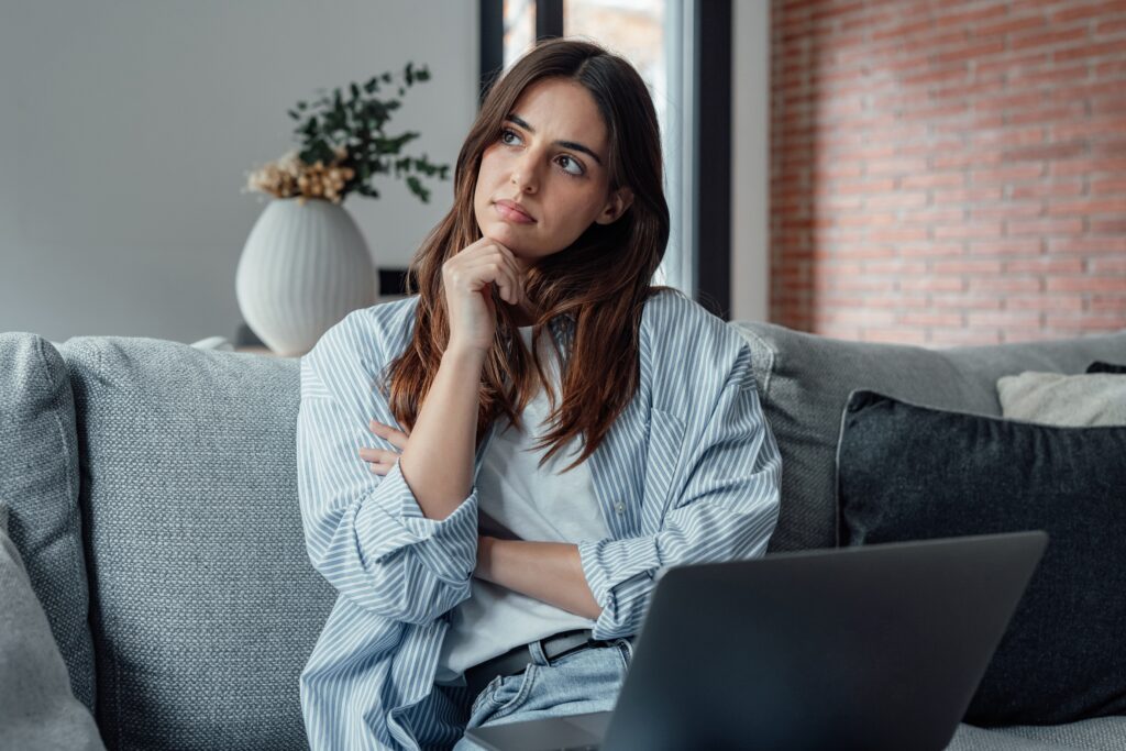 Thoughtful woman sitting on a couch with a laptop, considering whether SEO is worth it for small business growth.