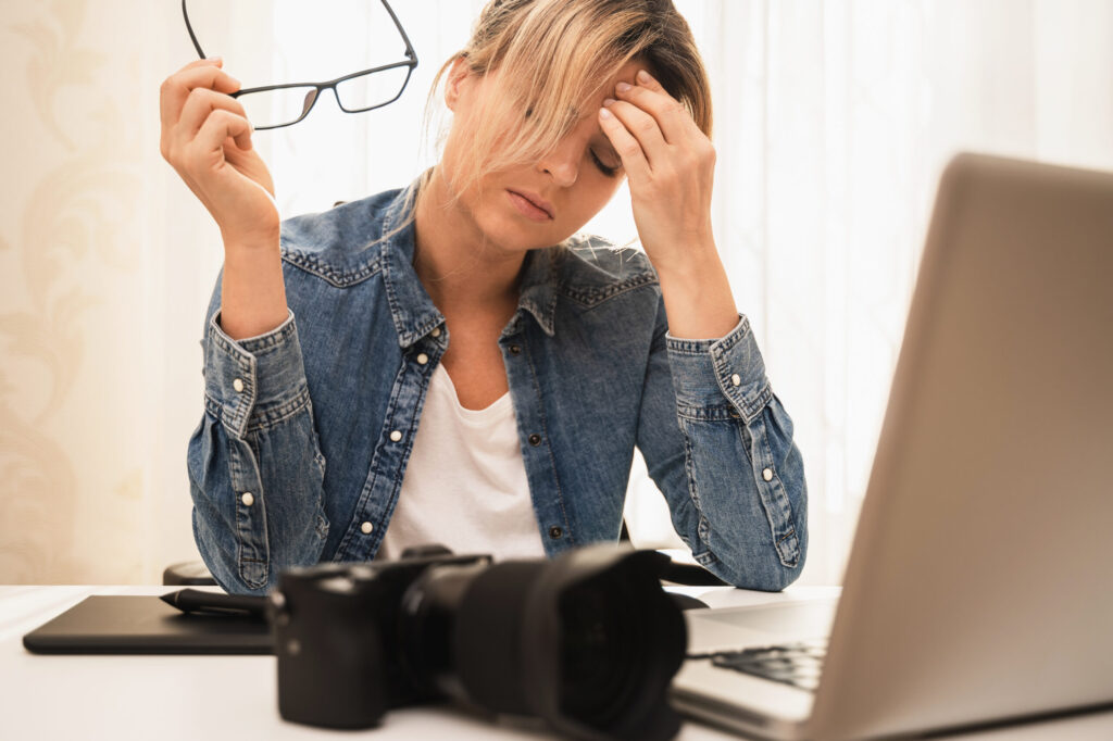 Frustrated photographer sitting at a desk with camera and laptop, realizing the need for SEO services for photographers to attract consistent bookings.