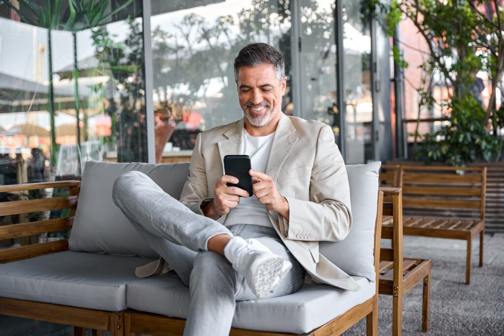 Confident man smiling while checking his phone outdoors, representing balance, positivity, and how to stay motivated in daily life.