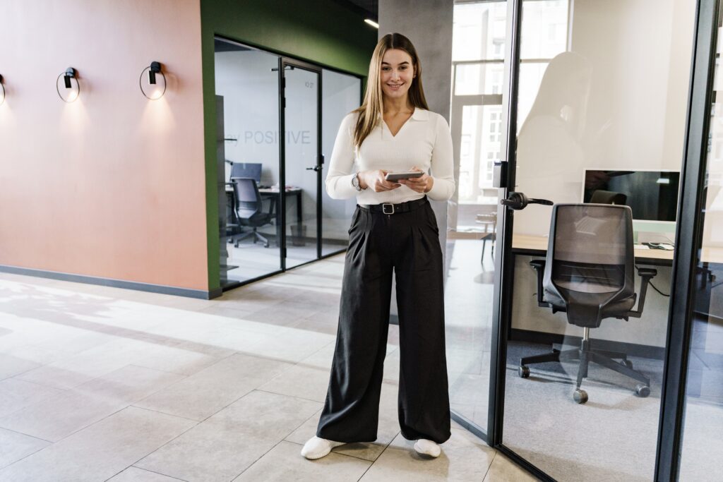 Confident Woman Standing in a Modern Office Holding a Tablet Representing Clarity Confidence and Focus the Qualities of a High Performer