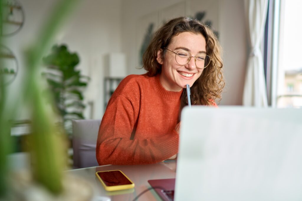 Smiling woman working from home on her laptop, feeling inspired and focused—illustrating how to stay motivated while pursuing goals.