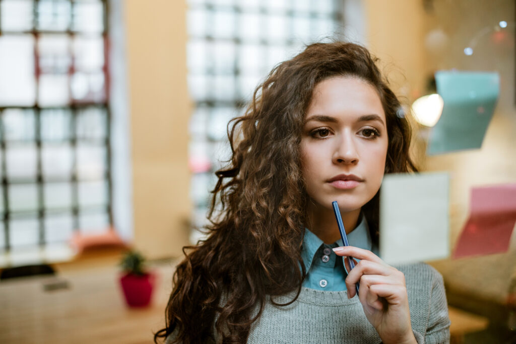 Focused Woman Holding a Pen and Thinking Deeply Representing Self reflection and Mindset Awareness As Part of Building a High Performance Identity