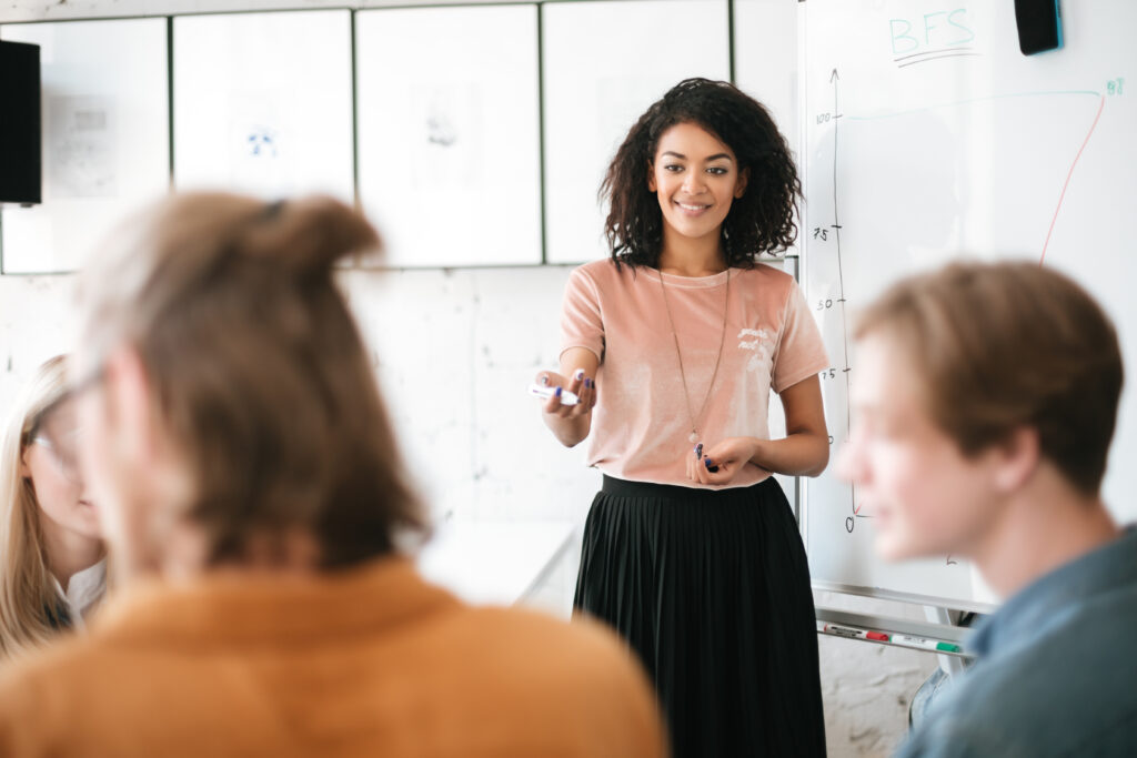 Confident Woman Leading a Presentation in Front of a Team Representing the Clarity and Leadership That Come from Developing a High Performance Identity