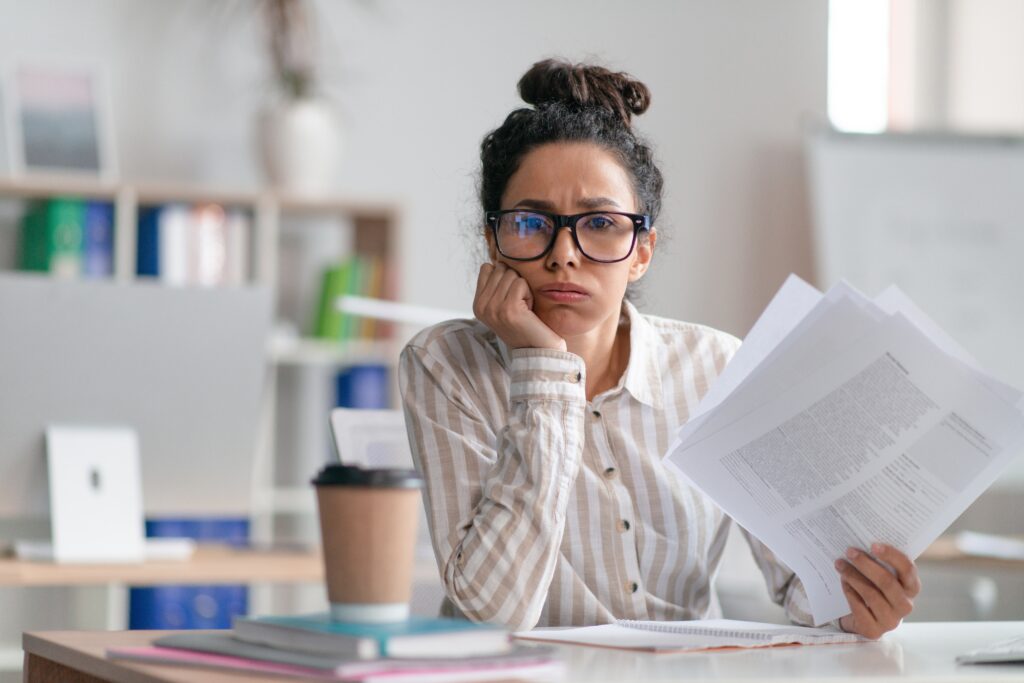 Frustrated woman sitting at desk with papers and coffee, realizing the need for high performance habits tools to improve focus and productivity.