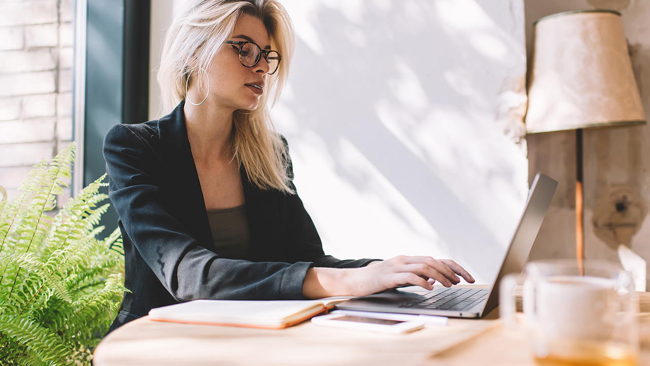 Focused woman working on a laptop in a bright office, representing clarity, growth, and productivity — the core benefits of high performance coaching.
